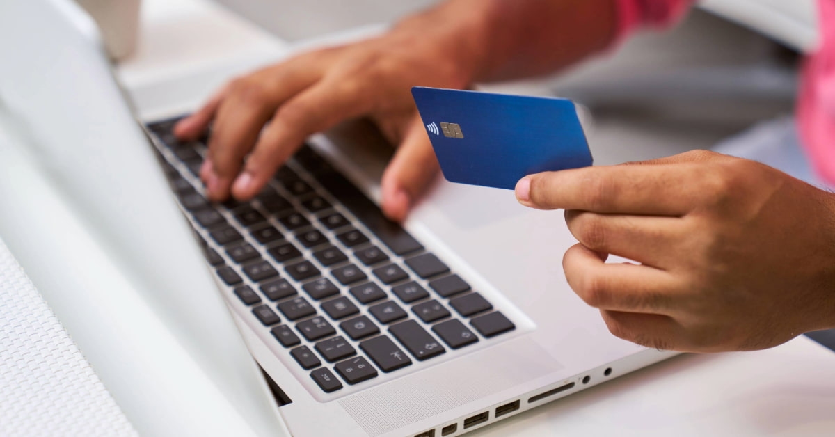 Homem segura cartão em frente a um notebook e pesquisa até que horas pode pagar boleto